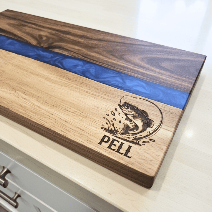 Wooden cutting board with blue resin strip and engraved fish design on a white surface