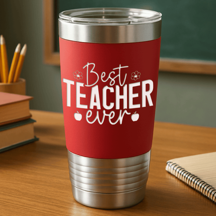 red teacher tumbler with 'best teacher ever' engraved in white sitting on a teacher's desk