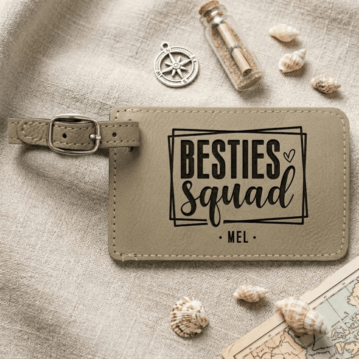 Beige luggage tag with 'BESTIES Squad' text on a textured surface with shells and a map.