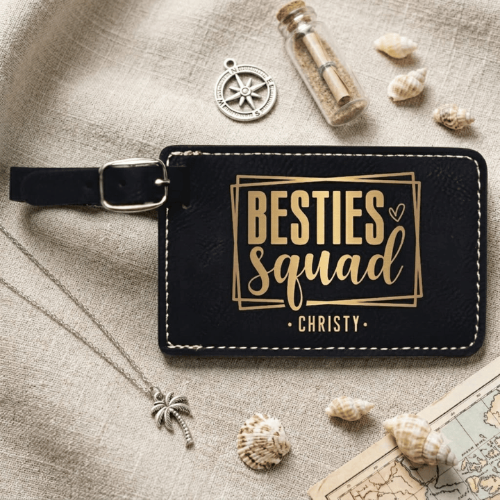 Black luggage tag with 'Besties Squad' text on a textured surface with decorative items.