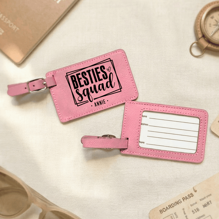 Pink luggage tag with 'besties squad Annie' engraved in black on the front and the back has clear plastic opening with space to write personal information.