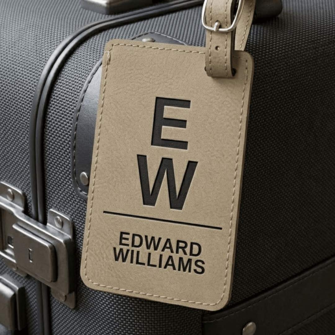 Light brown luggage tag with initials and name engraved in black attached to a black suitcase
