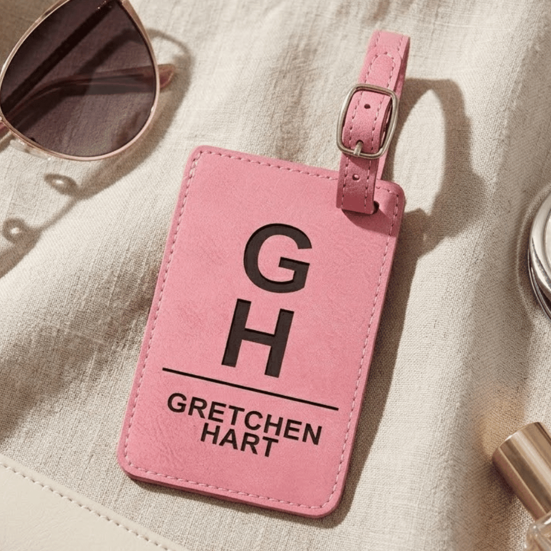 Pink luggage tag with 'Gretchen Hart' monogram engraved in black on a light fabric background