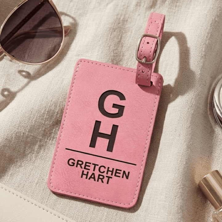 Pink luggage tag with 'Gretchen Hart' monogram engraved in black on a light fabric background