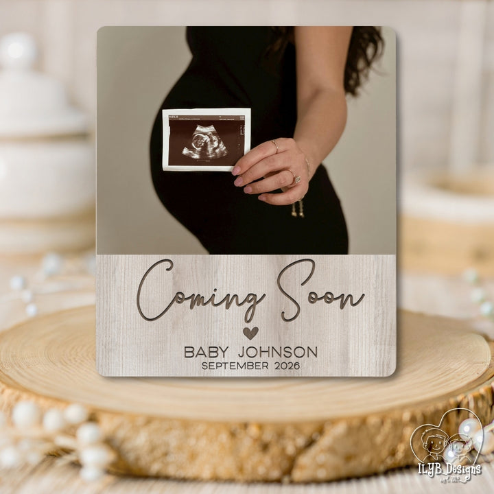 Pregnant belly with ultrasound photo and 'Coming Soon' announcement photo baord plaque on a wooden surface.