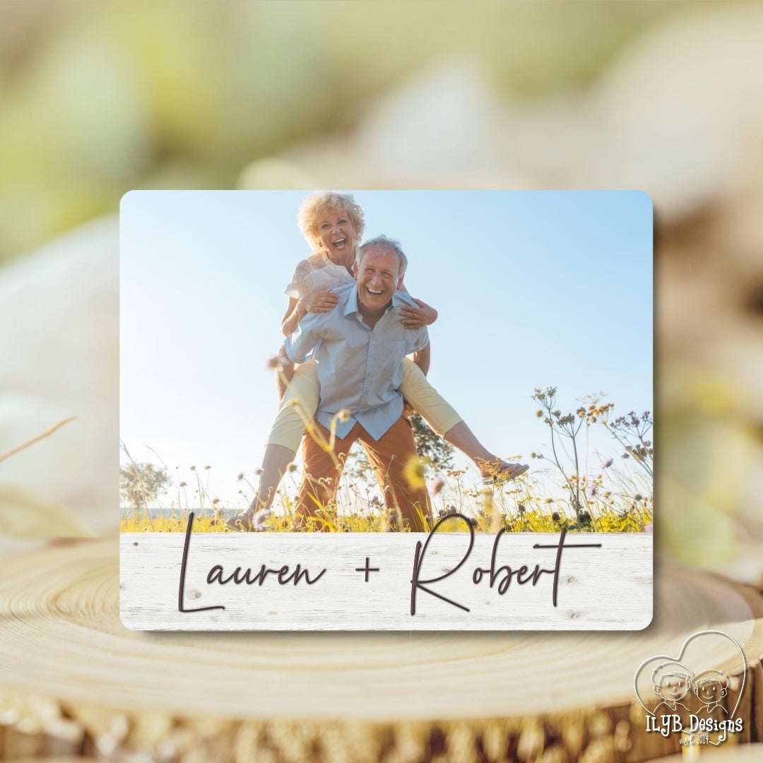 Wood photo plaque with a photo of an older couple in a field and 'Lauren + Robert' text, on a wooden surface.