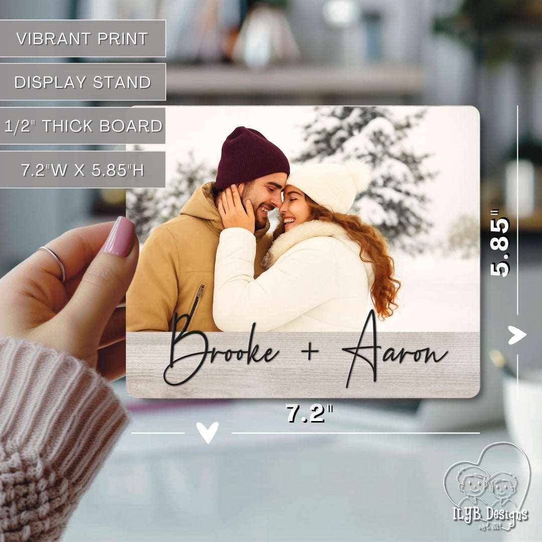 Wood photo plaque with a couple in winter clothing and 'Brooke + Aaron' text, held by a hand.