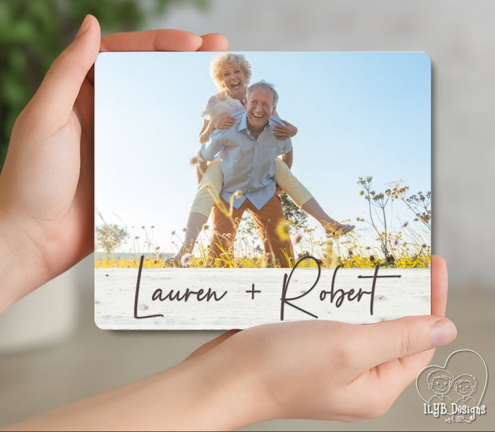 Hand holding a photo card with 'Lauren + Robert' and a couple in a field.