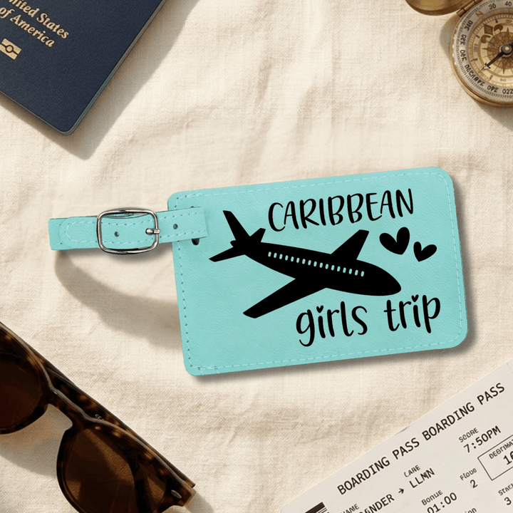 Turquoise luggage tag with airplane and 'Caribbean girls trip' text on a beige surface with travel items.