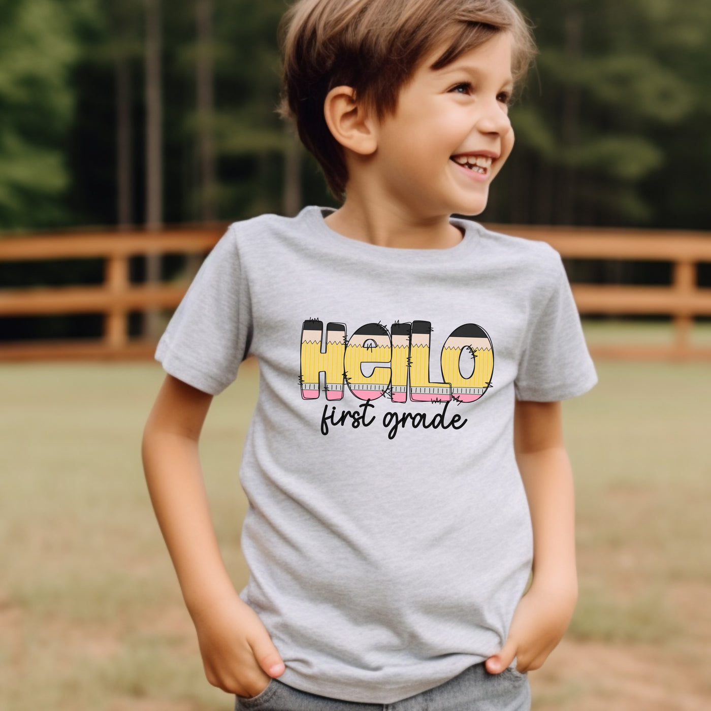 Young boy wearing athletic heather gray personalized school shirt that says hello in pencil shaped letters and first grade in black script underneath.