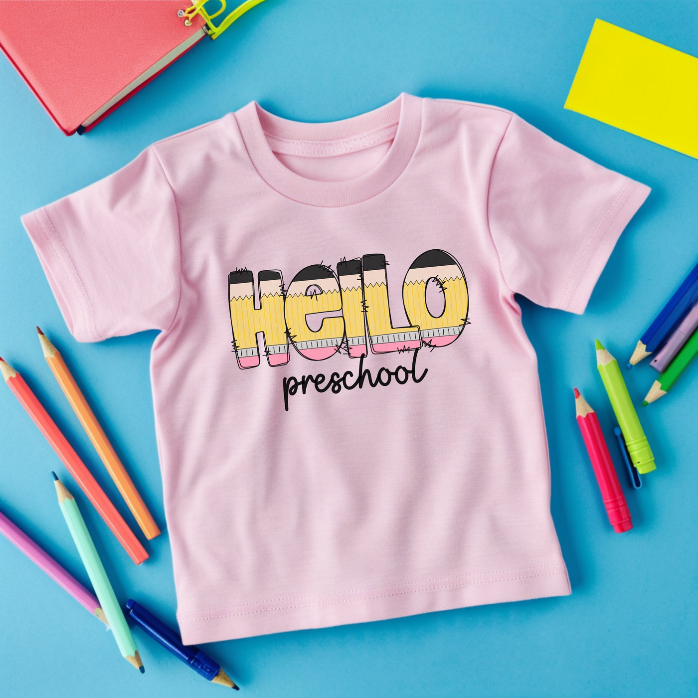 Light pink personalized school shirt that says hello in pencil shaped letters and preschool in black script underneath.