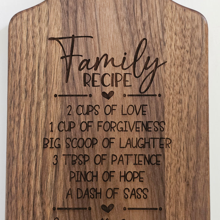 A wooden cutting board with a rounded top edge, featuring a dark engraved recipe titled &
