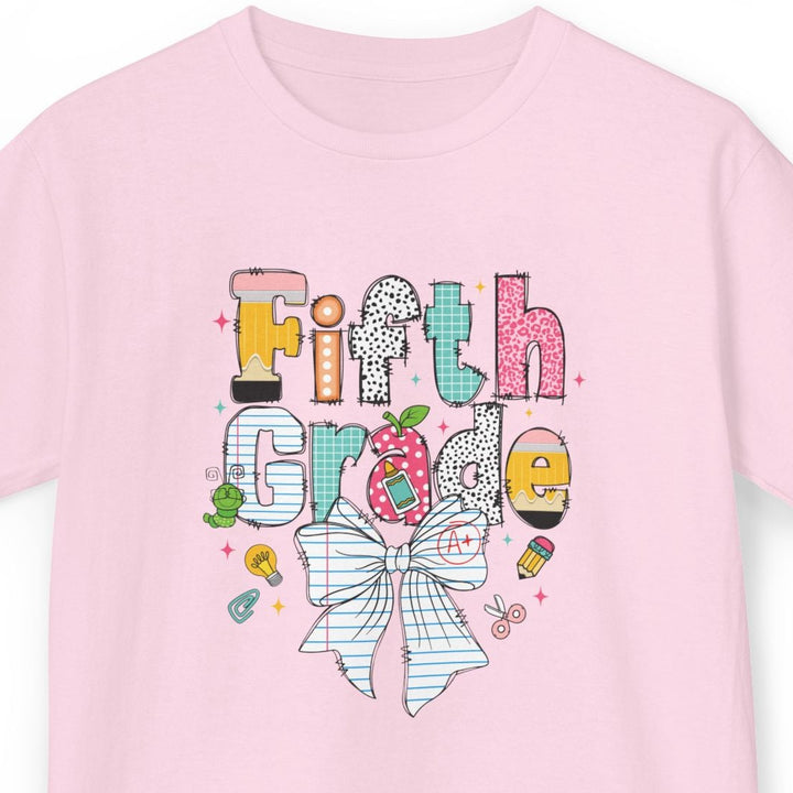 A light pink short-sleeve t-shirt with a colorful graphic on the front that reads 'Fifth Grade' in playful, decorated letters with a striped bow illustration below, shown on a plain white background.