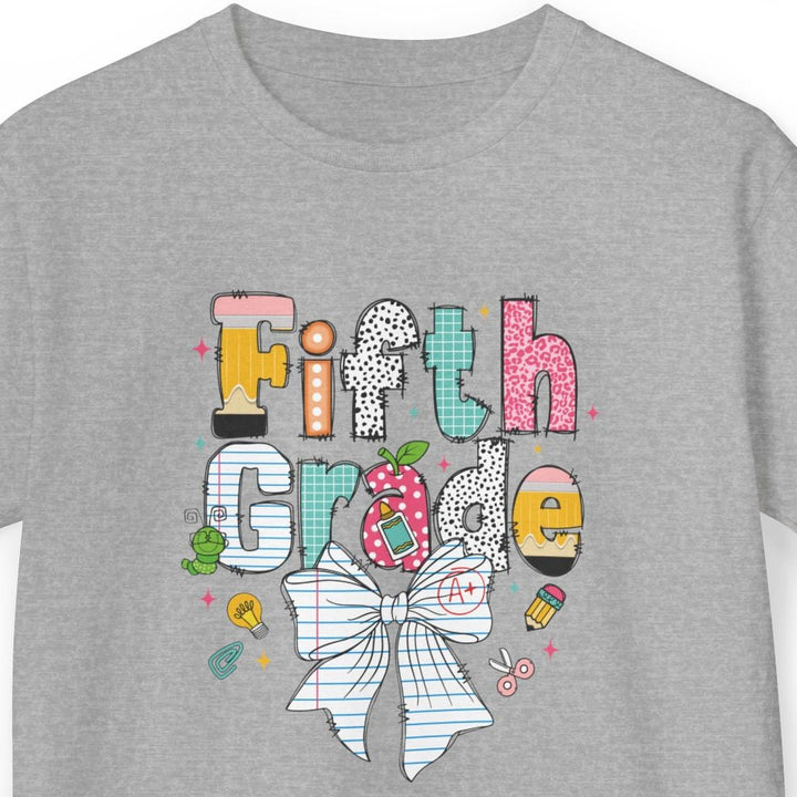 A heather gray short-sleeve t-shirt with a colorful graphic on the front that reads 'Fifth Grade' in stylized letters, featuring a striped bow, a pink polka-dots, a yellow highlighter, and small doodles, shown on a plain white background.