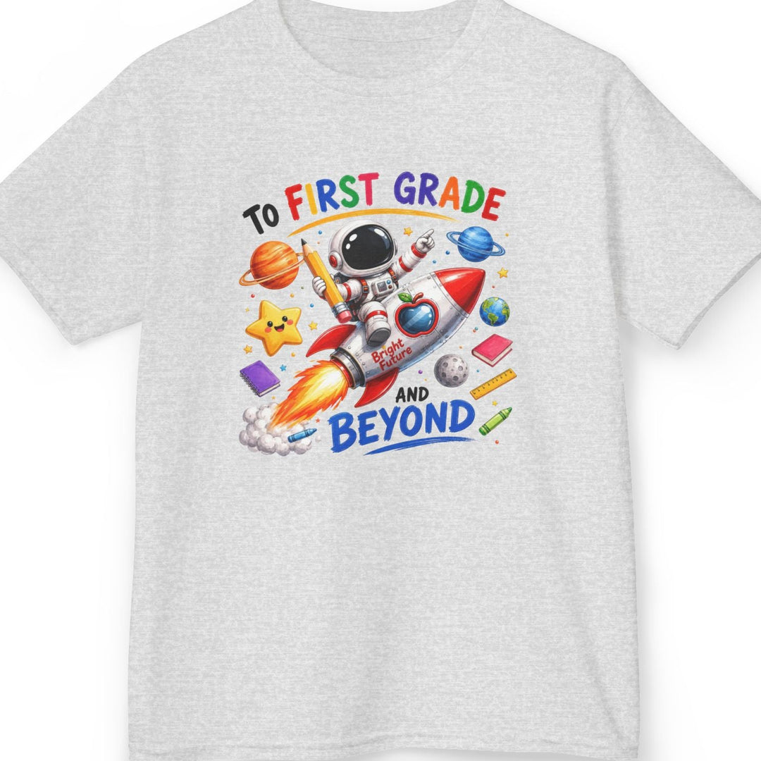 A light ash gray short-sleeve t-shirt with a colorful graphic on the chest featuring an astronaut, a rocket ship, planets, and the text 'TO FIRST GRADE AND BEYOND'.