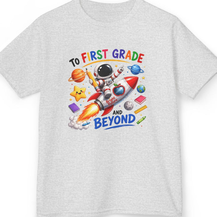 A light ash gray short-sleeve t-shirt with a colorful graphic on the chest featuring an astronaut, a rocket ship, planets, and the text 'TO FIRST GRADE AND BEYOND'.