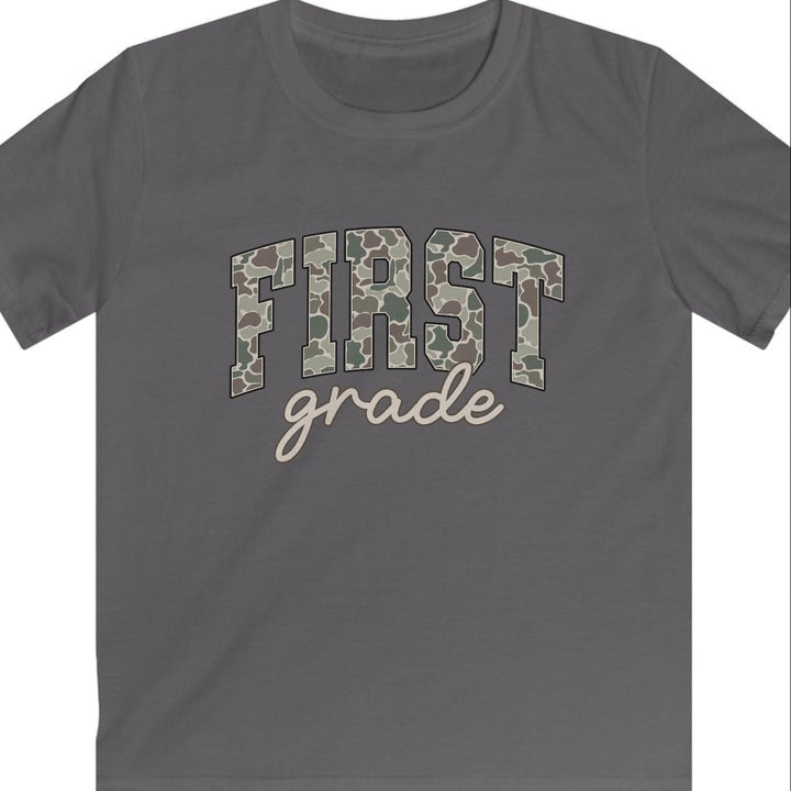 A dark gray short-sleeve t-shirt with 'FIRST grade' printed on the chest. The word 'FIRST' is in a camouflage pattern, and 'grade' is written below in a light beige cursive font, set against a plain white background.
