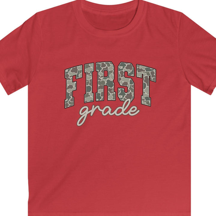 A red short-sleeve t-shirt with 'FIRST grade' printed on the chest. The letters in 'FIRST' are filled with a green and gray camouflage pattern, and 'grade' is written below in white cursive script.
