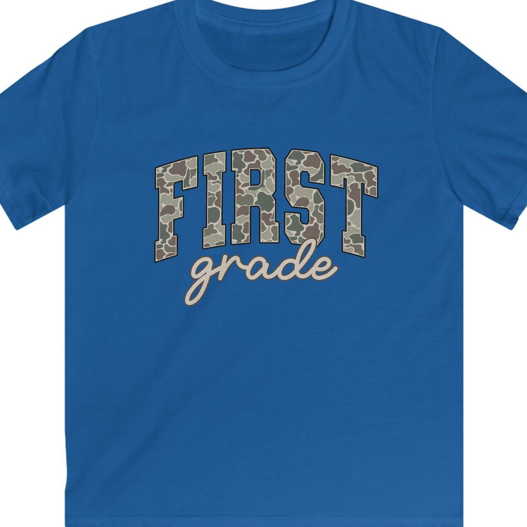 A royal blue short-sleeve t-shirt with 'FIRST grade' printed on the chest. The letters in 'FIRST' are filled with a brown and beige camouflage pattern, and 'grade' is written below in a light beige cursive font.