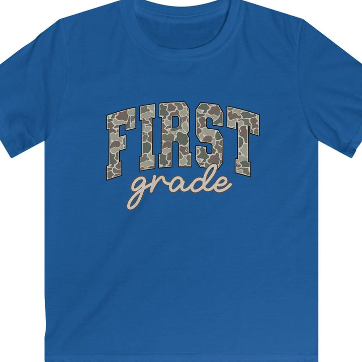 A royal blue short-sleeve t-shirt with 'FIRST grade' printed on the chest. The letters in 'FIRST' are filled with a brown and beige camouflage pattern, and 'grade' is written below in a light beige cursive font.