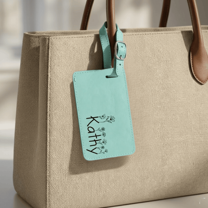 Beige handbag with a teal luggage tag featuring the name 'Kathy' engraved in black.