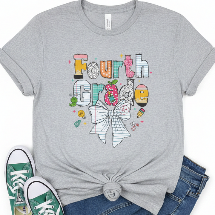 A heather gray graphic T-shirt laid flat with a knot at the hem, styled with blue jeans and green sneakers on a white background. The shirt features a colorful 'Fourth Grade' school-themed graphic with an apple, bow, and small doodles.