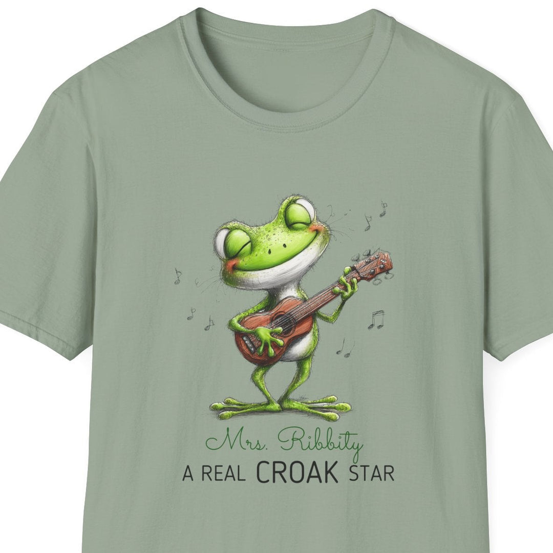 A sage green short-sleeve crewneck t-shirt featuring a cartoon frog playing a guitar with the text 'Mrs. Ribbity A REAL CROAK STAR' printed on the front, shown against a plain white background.