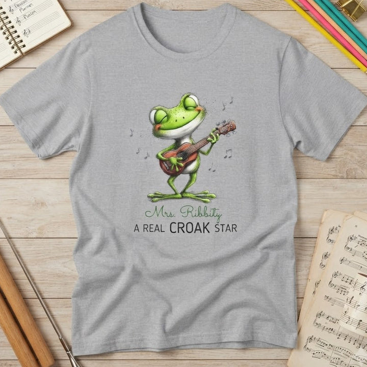 A light gray short-sleeve t-shirt with a cartoon frog playing a guitar and the text 'Mrs. Rabbity A REAL CROAK STAR' printed on the front.