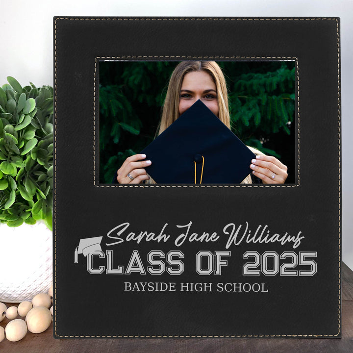 Graduation-themed photo frame with a personalized name, class year, and name of school on a wooden surface.
