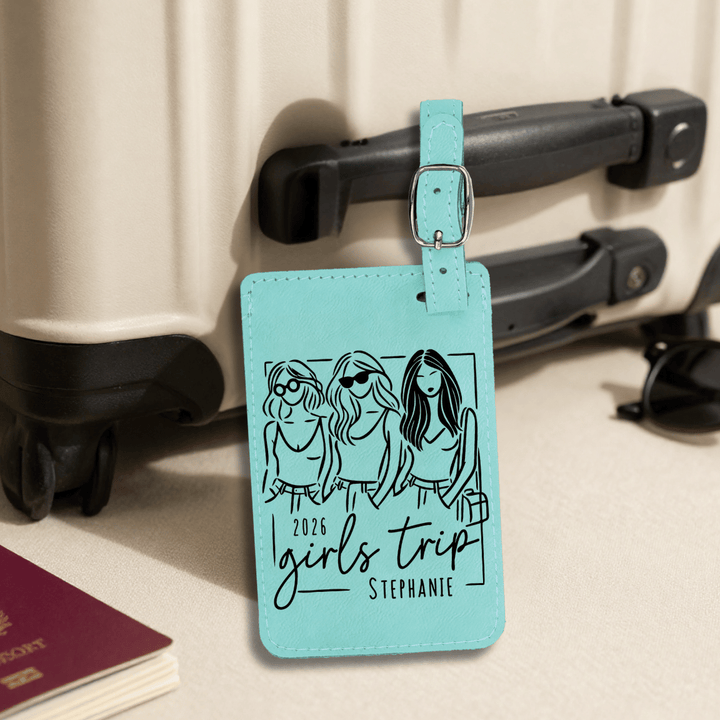 Turquoise luggage tag with '2026 Girls Trip Stephanie' design attached to a suitcase.