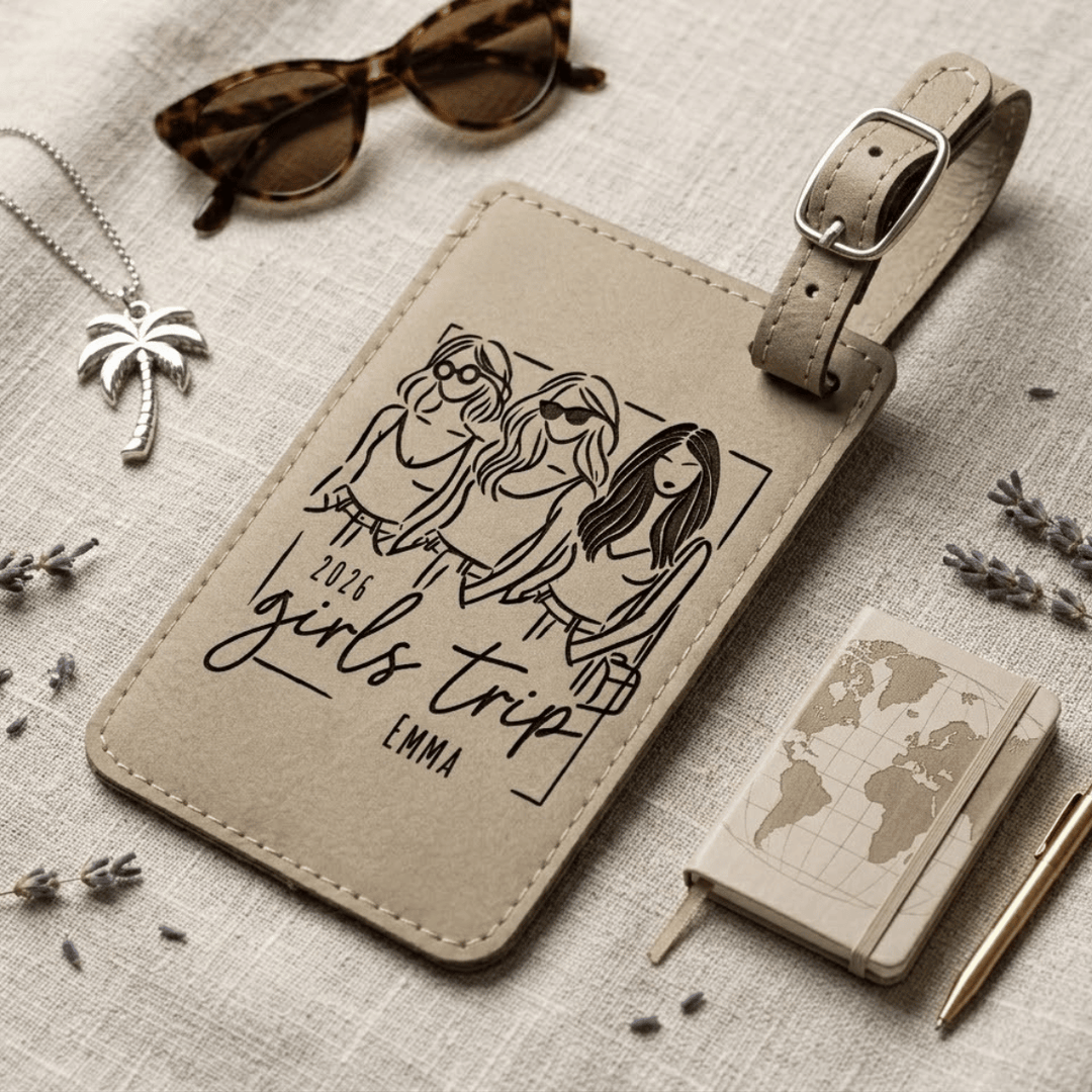 Beige luggage tag with '2023 girls trip' design on a textured surface with sunglasses and a notebook.