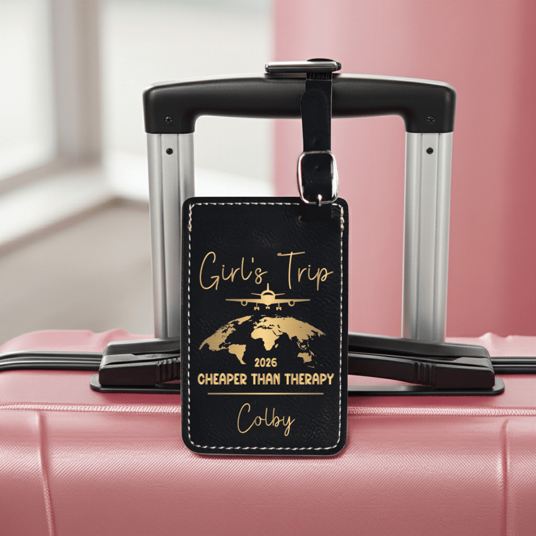 Black travel tag with gold text on a pink suitcase