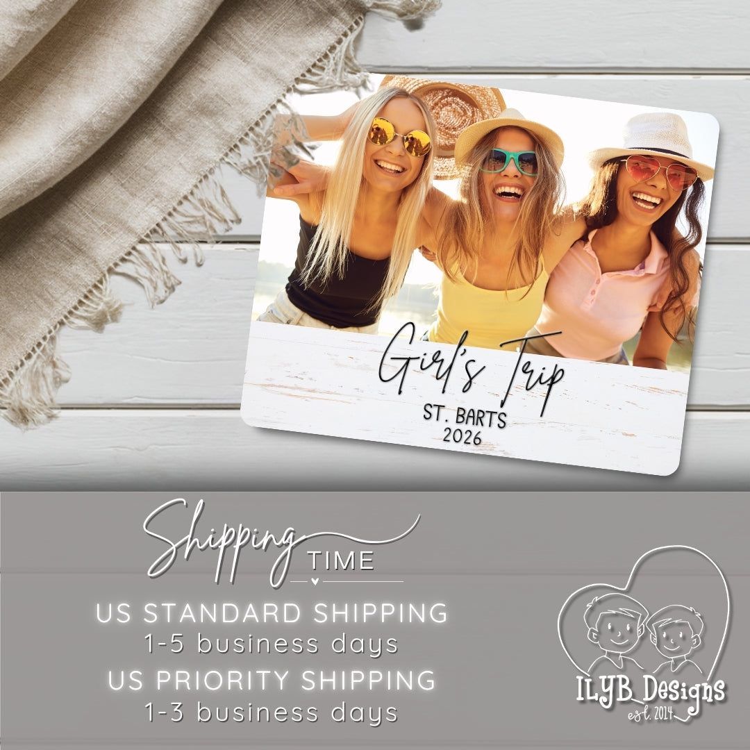 Photo plaque with three women on a beach, labeled 'Girls Trip St. Barts 2026', on a wooden surface with a blanket.