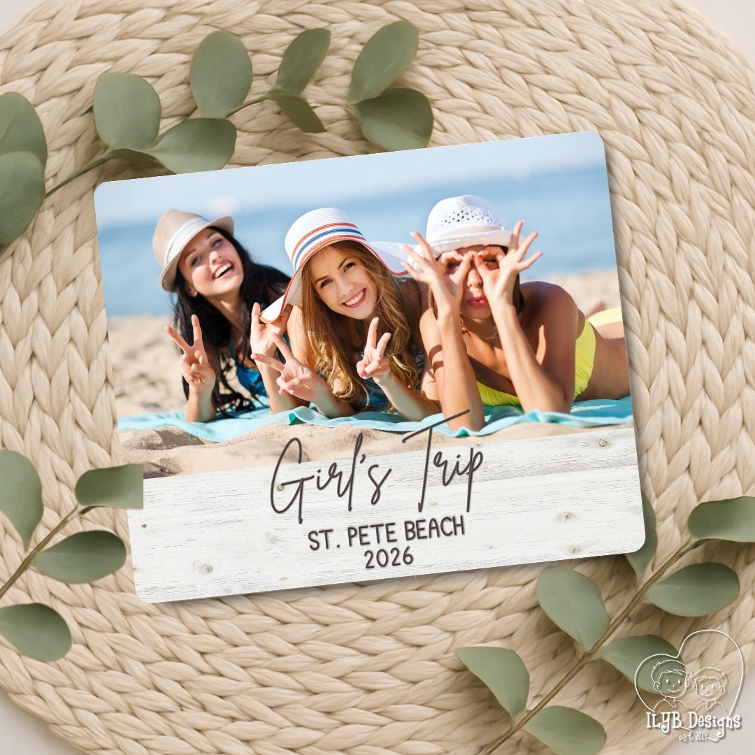 Photo board with a photo of three girls on a beach and text 'Girl's Trip St. Pete Beach 2026' on a woven surface with leaves.