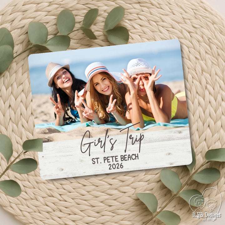 Photo board with a photo of three girls on a beach and text 'Girl's Trip St. Pete Beach 2026' on a woven surface with leaves.