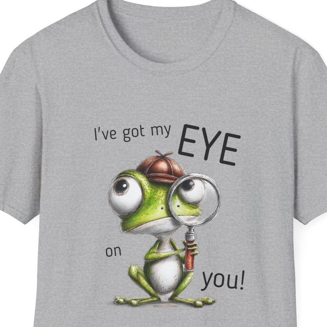 A light gray short-sleeve crewneck t-shirt featuring a cartoon graphic of a green frog wearing a brown hat and magnifying glass, with the text 'I've got my EYE on you!' printed on the front.