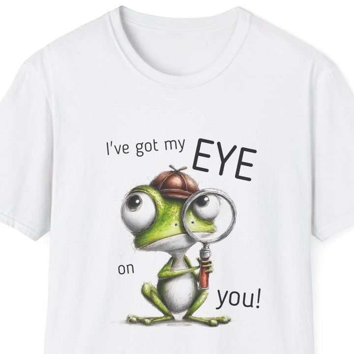A white short-sleeve crewneck t-shirt featuring a cartoon graphic of a green frog wearing a brown detective hat and magnifying glass, with the text 'I've got my EYE on you!' printed around it.