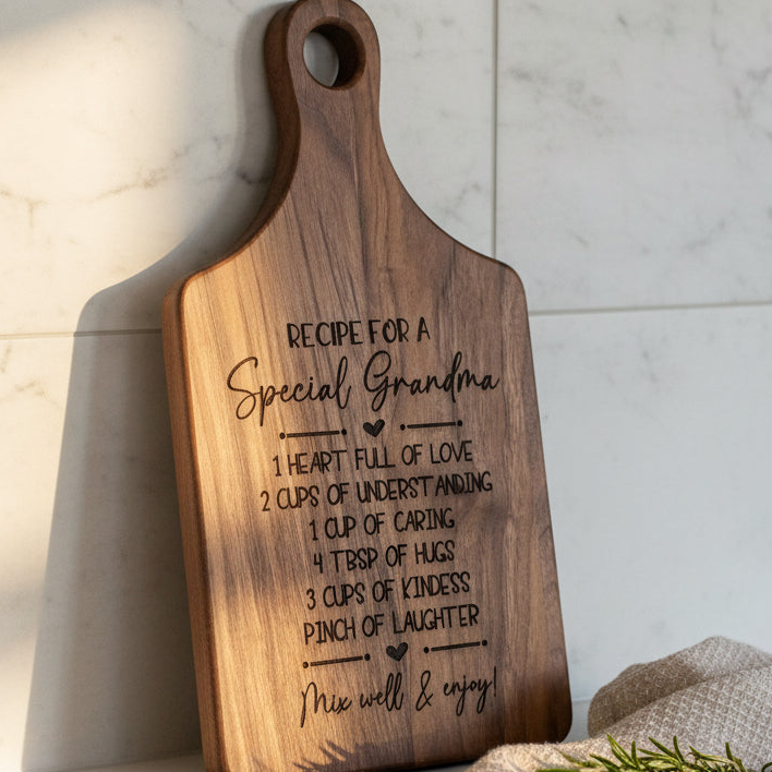 A wooden cutting board with a personalized engraved message for 'Special Grandma' resting against a white marble tile wall.