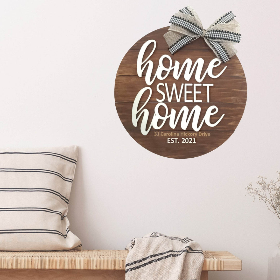 Decorative round wood sign in brown with 'home sweet home' text and a bow on top hanging on a wall above a wooden bench.