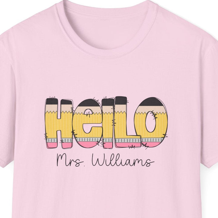 A light pink short-sleeve crewneck t-shirt featuring a graphic on the front that reads 'HELLO' in yellow pencil letters with black outlines and horizontal pastel stripes, with 'Mrs. Williams' printed below in black script.