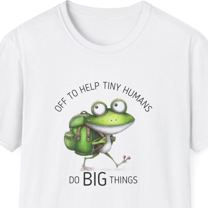 A white short-sleeve crewneck t-shirt featuring a cartoon graphic of a green frog wearing a backpack and the text 'OFF TO HELP TINY HUMANS' above and 'DO BIG THINGS' below.