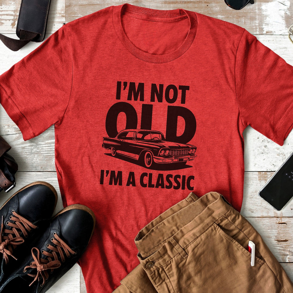 Red t-shirt with 'I'm not old, I'm a classic' text and car graphic on a wooden surface with shoes and pants.