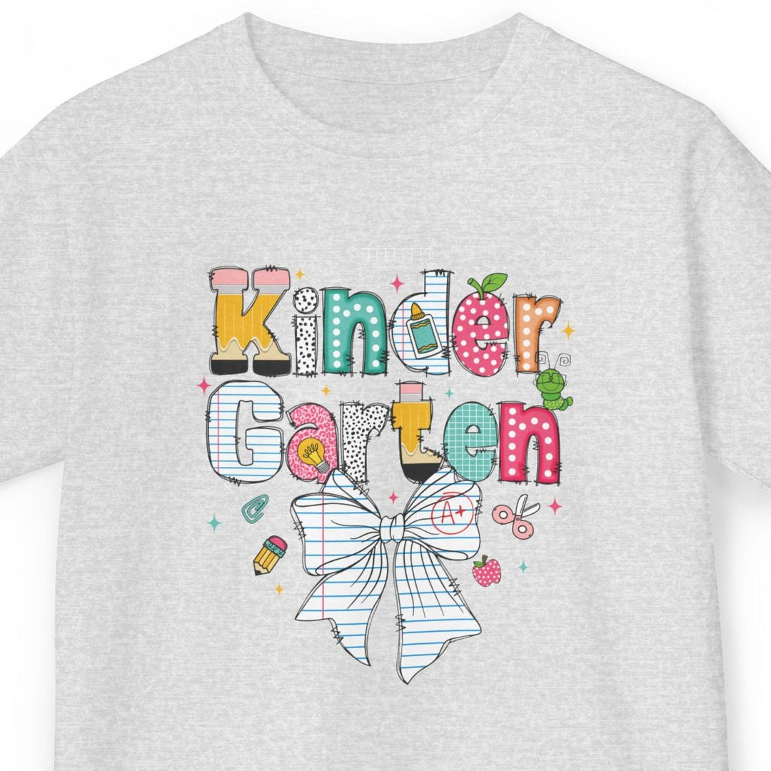 A light heather gray short-sleeve t-shirt with a colorful graphic on the front that reads 'Kinder Garten' in playful multicolored letters above a white bow illustration, shown on a plain white background.