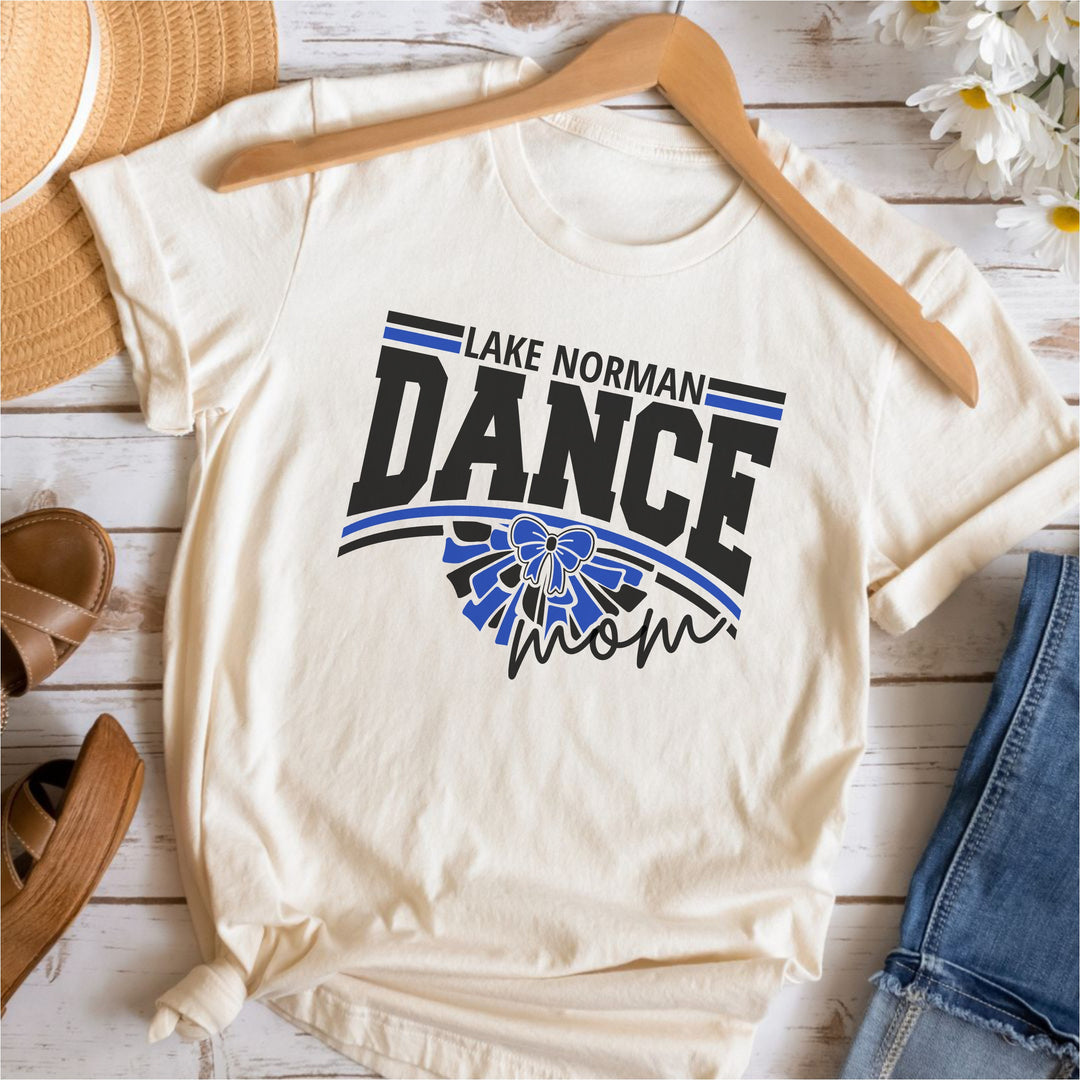 Sand t-shirt with 'Lake Norman Dance Mom' design on a wooden surface with accessories.