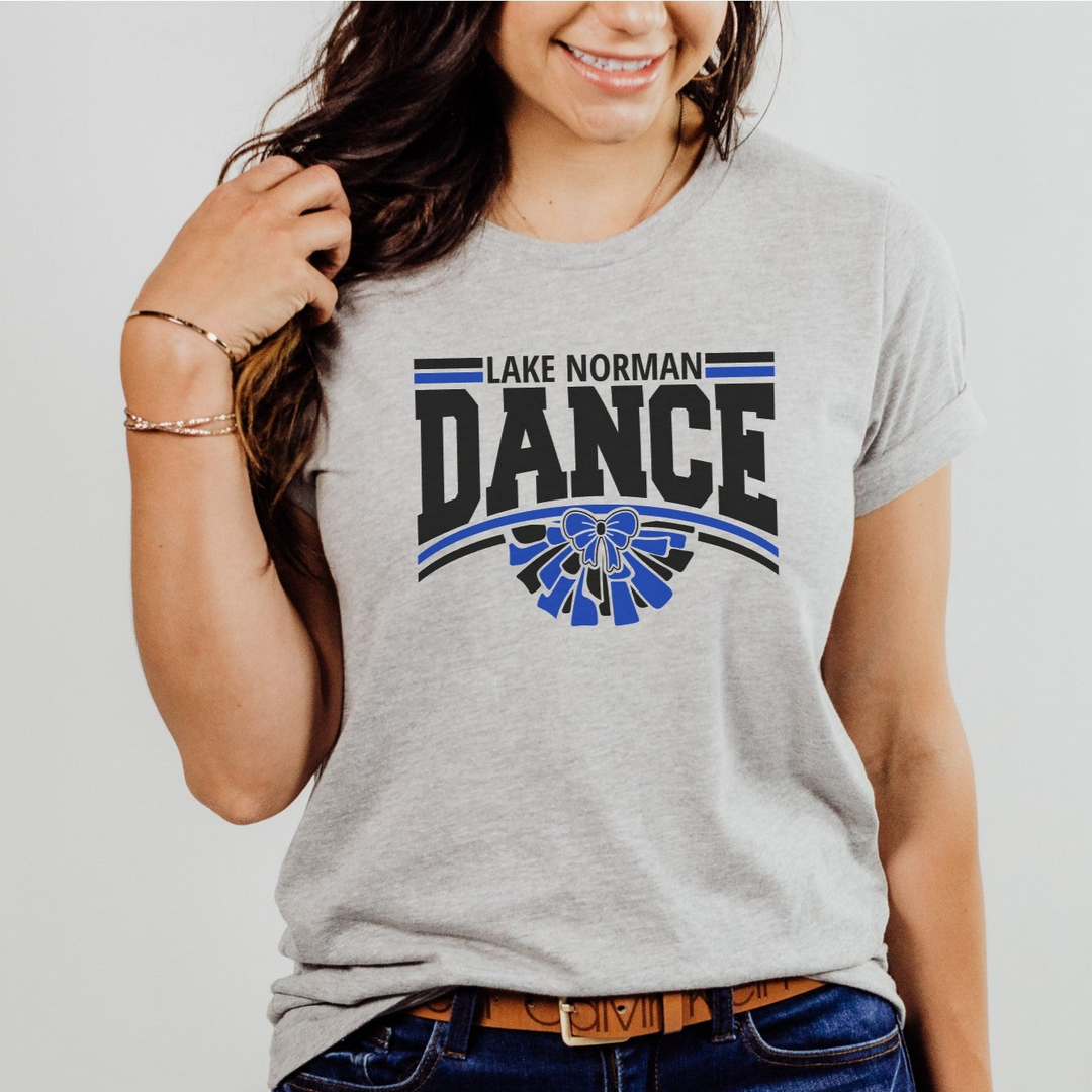 Girl wearing gray t-shirt with 'Lake Norman Dance' text and blue bow  and pom pom graphic, paired with blue jeans.