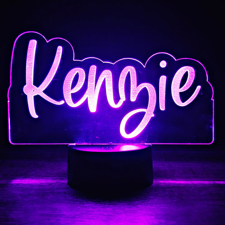 LED night light with the name 'Kenzie' engraved in a script font on acrylic lit in purple in a black background