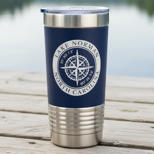 A navy blue insulated travel tumbler with a stainless steel lid and base, featuring a white circular Lake Norman North Carolina compass graphic on the front sitting on a rustic wood deck with lake in the background.