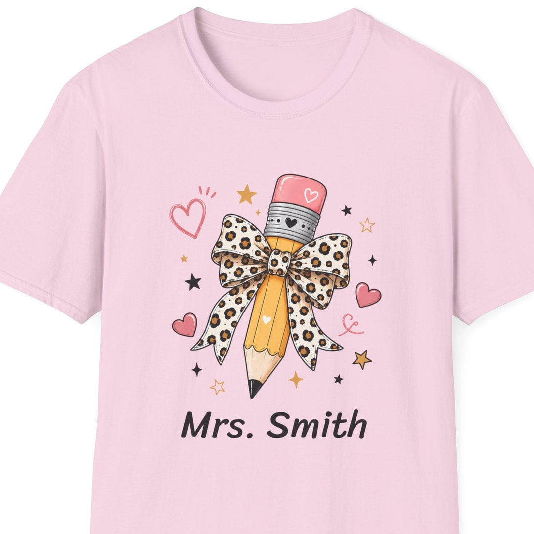A light pink short-sleeve crewneck t-shirt featuring a graphic of a pencil with a leopard-print bow, surrounded by small hearts and stars, with the text 'Mrs. Smith' printed below.