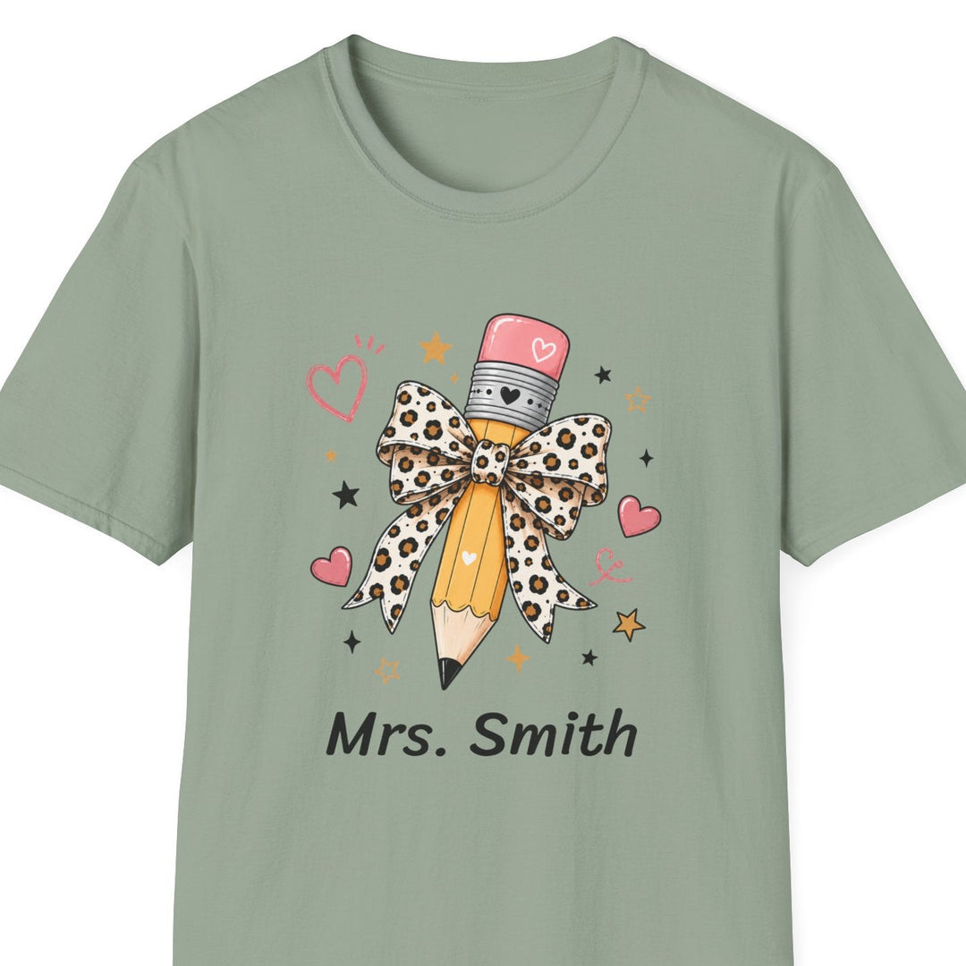 A sage green short-sleeve t-shirt with a custom graphic of a pencil wrapped in a leopard-print bow, surrounded by pink hearts and stars, with the text 'Mrs. Smith' printed below.