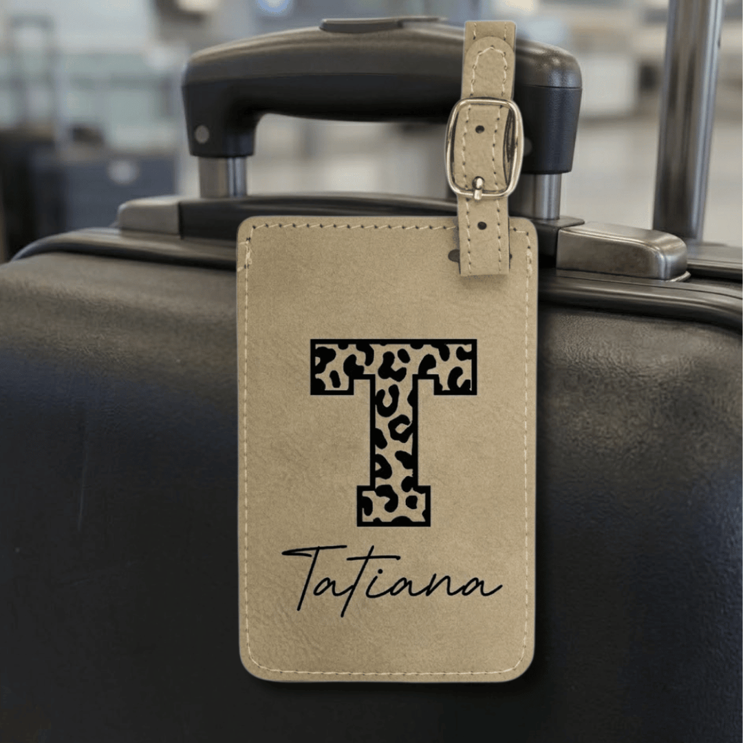 Luggage tag with leopard print letter 'T' and name 'Tatiana' engraved in black attached to a suitcase.